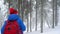 Funny tourist girl waving a hand to someone and walking on a winter snow-covered coniferous forest in the mountains