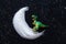Funny toy dinosaur stands on a white powder crescent moon. Black background. Fabulous concept of the theory of the origin and