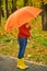Funny unrecognizable kid under an orange umbrella