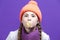 Funny Winsome Girl In Coral Knitted Seasonal Hat Posing With Chewing Gum Bubble In Front of Face Against Purple Seamless