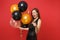 Funny woman in black dress celebrating blinking pointing index finger holding air balloons isolated on red background