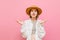 Funny woman in a hat looks puzzled at the camera with raised arms from the bewildered face on a pink background. Portrait of