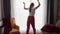 Funny woman in pajamas dancing at big window in living room. People relaxing at home, having fun, positive emotions and fun.
