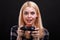 A funny young girl fascinatingly plays with joystick with a frightened look. On a black background.