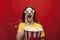 Funny young girl shocked in 3D glasses watching a movie and eating popcorn on a red colored background, she screams and popcorn