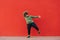 Funny young man with overweight and curly hair dances against the background of a red wall, looks at the camera and moves