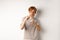 Funny young man with red hair raising fists for fight, shadow boxing and looking serious at camera, standing over white