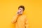 Funny young man with a runny nose uses nasal spray on a yellow background. The sick boy took off his mask to use an anti-cold