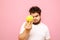 Funny young overweight man stands on a pink background, looks surprised at the apple in his hand and makes a funny face wearing a