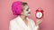 Funny young woman with alarm clock at morning. Girl with a mask on his face holds a clock on a pink background. Concept