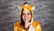 A funny young woman in a big pajamas of giraffe is smiling and doing silencing gesture with index finger at her lips on