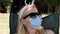 Funny young woman in a medical protective mask and sunglasses sits in a chair and rest in park. Covid-19 pandemic. Close-up