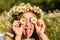 A funny young woman in a wreath of daisies is laughing and holding daisies in front of her eyes with her tongue hanging out. On a