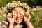 A funny young woman in a wreath of daisies is laughing and holding daisies in front of her eyes. On a large field of daisies