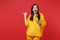 Funny young woman in yellow fur sweater pointing thumb aside, sing song in microphone isolated on bright red wall
