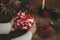 Furoshiki christmas gift. Hands holding christmas gift wrapped in red festive fabric on rustic wooden table with scissors, paper