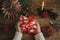 Furoshiki christmas gift. Hands holding christmas gift wrapped in red festive fabric on rustic wooden table with scissors, paper