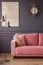 Furry pillow on a powder pink sofa, elegant golden sunburst mirror and marble painting on a dark gray wall in a living room inter