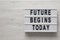 `Future begins today` words on a modern board on a white wooden background, top view. Overhead, from above, flat lay. Copy space