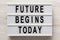 `Future begins today` words on a modern board on a white wooden surface, top view. Overhead, from above, flat lay. Close-up