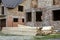 Future cottage under construction and pile of gravel and stack of boards in front of not finished new big brick house with brown