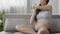 Future mother sitting on couch in headphones, stretching upper body, bodycare