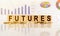 FUTURES the word on wooden cubes, cubes stand on a reflective surface, in the background is a business diagram