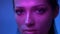 Futuristic fashion model with glitter makeup in purple neon lights blinking and watching peacefully into camera in