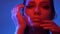 Futuristic fashion model in red and blue neon lights touching face with hands gently and glancing calmly into camera.