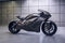 A futuristic titanium electric motorcycle in a garage with concrete floor and wall