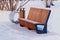 Futuristic wooden bench with an urn in a snowy winter park on a snow-cleared site.