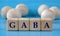 GABA - word on wooden cubes on a blue background with wooden round balls