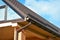 Gable roofing construction with brown metal tiled roof, a rain gutter, snow guards and a skylight against blue sky