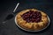 Galette with ripe red cherry filling and cake server on dark blue background. Homemade sweet open pie