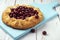 Galette with ripe red cherry filling with napkin on blue cutting board. Homemade sweet open pie on white wooden background