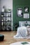 Gallery of black and white poster on green wall behind king size bed with pillows and blanket