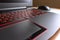 Game laptop with red colored keyboard and a mouse on background