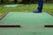 a game of mini-golf, a view from the hole at the time of striking a yellow ball with a stick