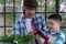 Gandpa assist grandchild wearing glove while planting small tree flower together at greenhouse. Senior man grandparent wear