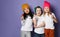 Gang of three cool kids in white t-shirts, colorful hats and pants posing with lollipops hugging together on purple