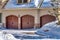 Garage entrance with snowy driveway leading to three arched wooden garage doors