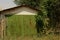 Garage with green iron rusty gate overgrown with vegetation and grass