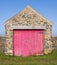 Garage made of Welsh stone with worn pink wooden doors. UK