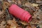 Garbage from a dirty old red plastic bottle of a thermos lies in brown dry fallen leaves