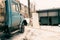 A garbage truck stands in front of containers of household waste and a door dusted with snow and a picture of a heart on it