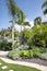 Garden corner featuring palm trees and lots of luxuriant plants, with a neat stone path crossing through the well-kept grass