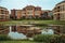 Garden with fancy brick building reflected to wide pond in a cloudy day at Weesp.