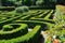 A garden featuring a labyrinthine maze in the middle surrounded by various plants and flowers, An elaborate maze of hedges in an