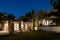 Garden with an old building on the right and a new house on the left. Nighttime scene with all the lights turned on