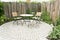 Garden patio with two chairs and round table in front of flowerbed and wooden planks